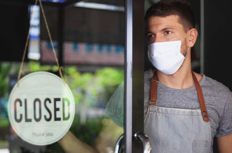 business owner standing in doorway with a closed sign